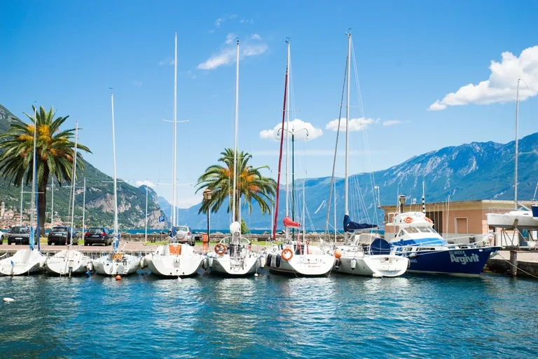 Segelboote am Steg eines Hafens mit Palmen und Bergen im Hintergrund