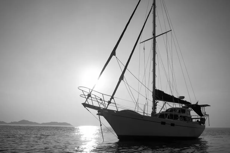 Segelyacht vor Anker im Gegenlicht, die Ankerkette läuft vom Bug ins Wasser